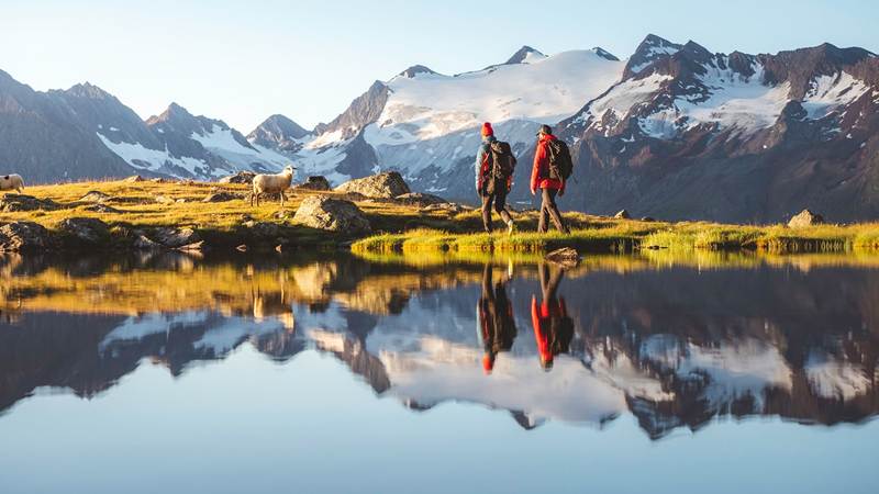 Zwei Menschen wandern einen Bergsee entlang.